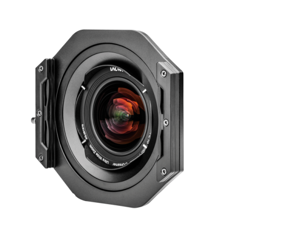 Lähikuva NiSi-suodattimen pidikkeestä (100mm) Laowa 10-18mm f/4.5-5.6 -levysuodin pidikkeestä kiinnitettynä objektiiviin, eteenpäin päin, tavallista valkoista taustaa vasten, jossa on näkyviä lasielementtejä ja värikkäitä heijastuksia.