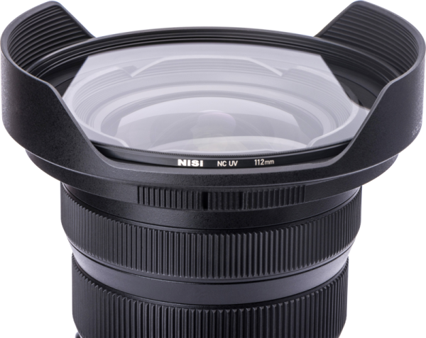 Lähikuva mustasta kameran objektiivista, jossa on laajakulmahuppu ja NiSi NC UV 112mm Filter For Nikon Z 14-24mm f/2.8 -UV suodin -etiketti suodattimessa valkoista taustaa vasten.