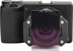 Musta digitaalikamera, jossa on NiSi Master Kit For Ricoh GR IIIx, jonka etupuolelle on kiinnitetty suodatinpidike ja suorakulmainen gradienttilinssi-suodatin, kuvassa eteenpäin valkoista taustaa vasten.