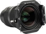 Close-up of a professional camera lens with NiSi Square Black Mist 1/4 100x100mm filter in a square holder. The black lens has textured focus rings and visible glass elements, and the clear filter is attached to the front.