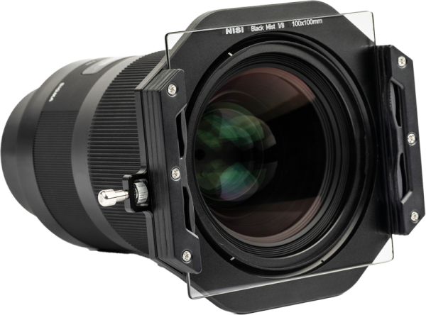Close-up of a professional camera lens with NiSi Square Black Mist 1/4 100x100mm filter in a square holder. The black lens has textured focus rings and visible glass elements, and the clear filter is attached to the front.