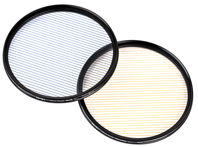 Kaksi päällekkäistä NiSi Filter Allure Streak Blue 2mm 82mm -suodinsuodinta lepää tavallisella pohjalla; vasemmassa näkyy sininen sävy, jossa on diagonaalisia mustia viivoja, ja oikeassa näkyy oranssi sävy, jossa on samanlaisia diagonaalisia mustia viivoja.