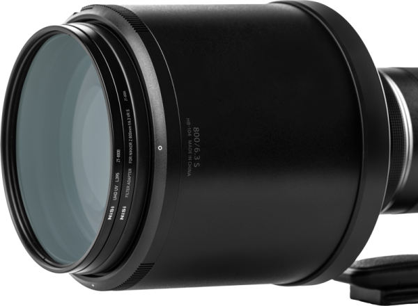 Lähikuva NiSi-suodattimesta UHD UV L395 Nikkor Z 800mm f/6.3 VR S:lle, jossa näkyy yksityiskohtainen teksti reunassa ja näkyvät lasielementit tavallista taustaa vasten.