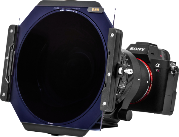 Sony Alpha -kamera, jonka etupuolelle on kiinnitetty NiSi Filter Holder S6 Kit True Color for Sigma 14mm f/1.4 DG DN -suodatin, kiinnitetty kolmijalka-adapteriin, eristetty valkoiselle taustalle.