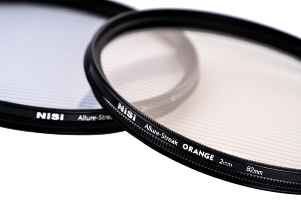 Lähikuva kahdesta kameran linssisuodattimesta, joissa on hienoja raitakuvioita päällekkäin valkoisella pohjalla. Toisessa suodattimessa on merkintä "NiSi Filter Allure Streak Blue 2mm 67mm -suodin" ja toisessa on samanlainen kuvio.