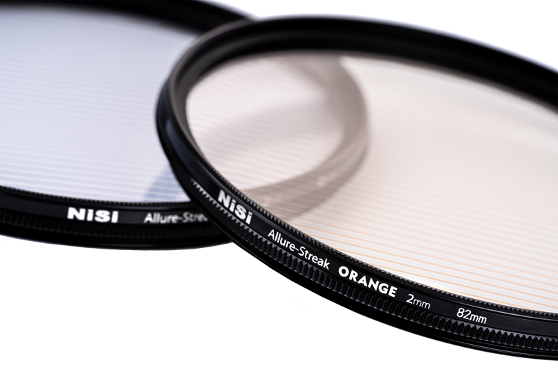 Lähikuva kahdesta kameran linssisuodattimesta, joissa on hienoja raitakuvioita päällekkäin valkoisella pohjalla. Toisessa suodattimessa on merkintä "NiSi Filter Allure Streak Blue 2mm 67mm -suodin" ja toisessa on samanlainen kuvio.
