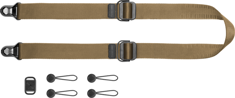 Peak Design Slide Lite v3 Coyote -kamerahihna on vaalealla pohjalla esitetty ruskehtava säädettävä nailonhihna, jossa on mustat metalliosat, kaksi pikakiinnikettä ja neljä silmukkaliitintä.