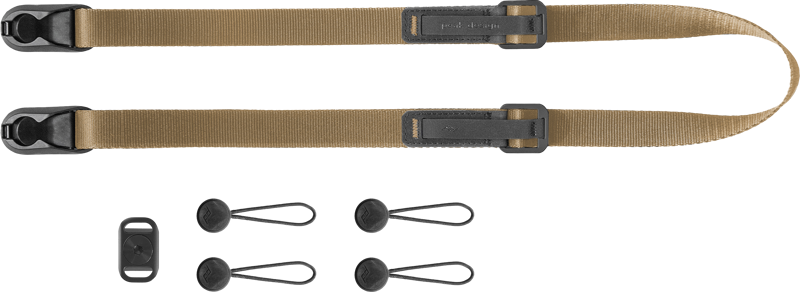 Peak Design Leash Coyote -kamerahihna on ruskehtava säädettävä kamerahihna, jossa on mustat laitteistot, neljä mustaa ankkurikiinnikettä ja suorakulmainen musta kiinnitysklipsi, joka näkyy tavallisella pohjalla.