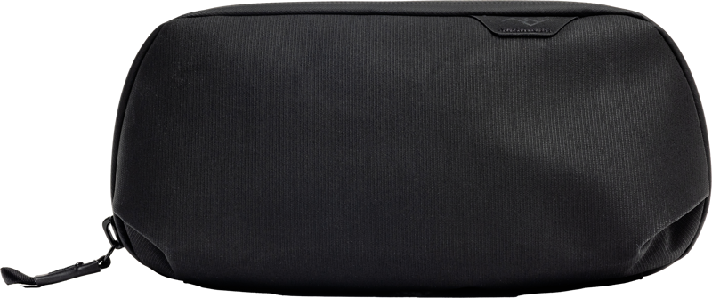 The black Peak Design Tech Pouch Small has a smooth texture, minimal branding and a small tag next to the zipper against a light background.