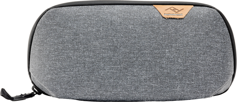 The Peak Design Tech Pouch Small in Charcoal features grey textured fabric, a black zip closure and tan leather logo accents in the top right corner against a white background.