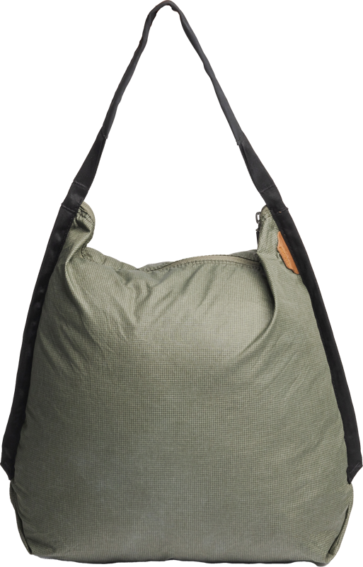 Peak Design Packable Tote in Sage on tilava, vaaleanvihreä kangaskassi, jossa on leveä musta olkahihna ja ruskea sivulappu valkoisella pohjalla.