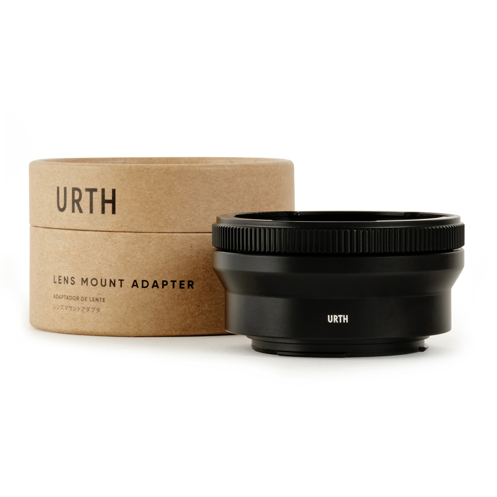 The black Urth Pentacon Six (P6) - Canon (EF / EF S) Lens Mount Adapter is shown next to its cylindrical brown cardboard box that reads Lens Mount Adapter, both against a white background.