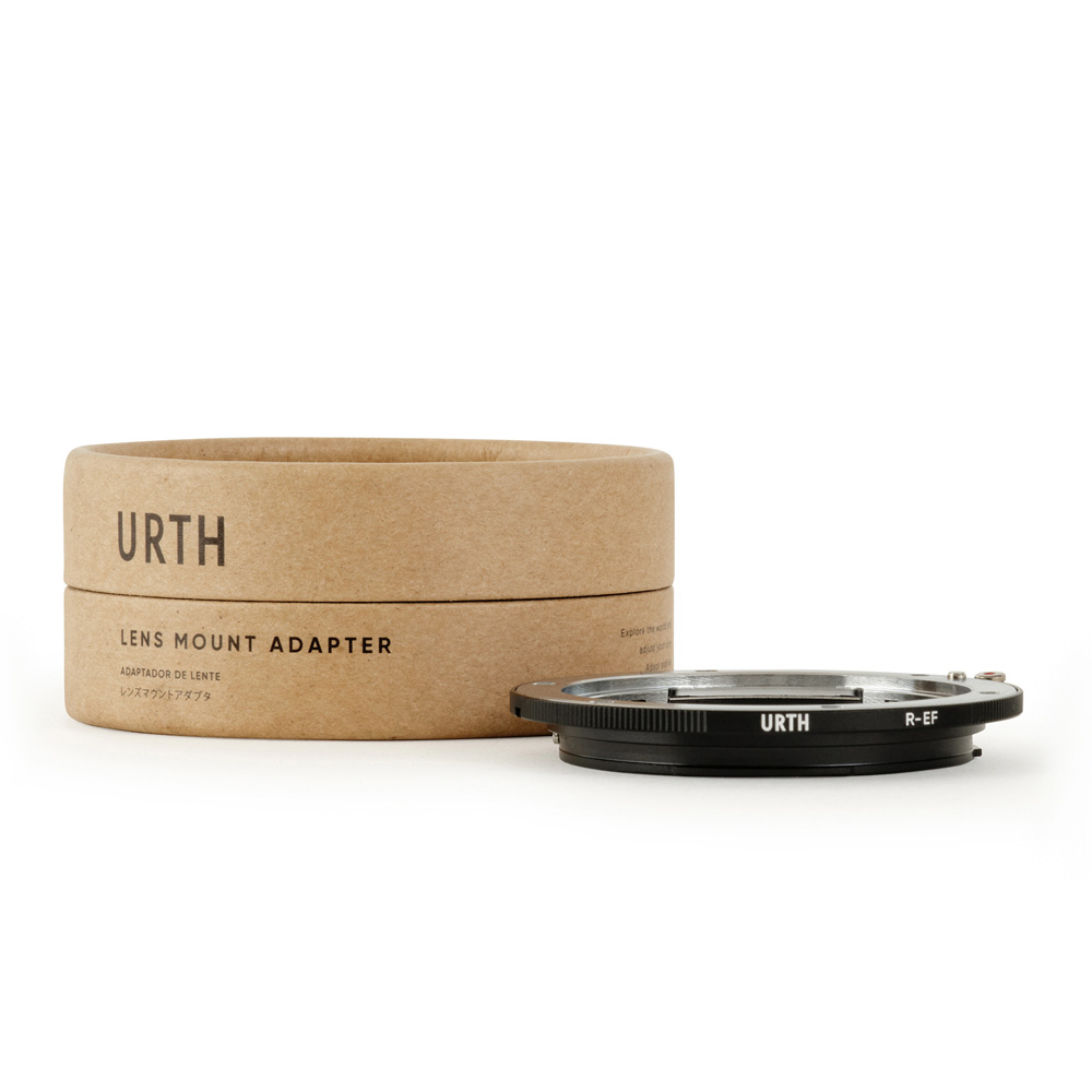 Urth Leica R - Canon (EF / EF S) objektiiviadapteri ja sen sylinterimäinen vaaleanruskea pahvipakkaus, jossa on musta teksti, näkyvät valkoisella pohjalla. Mustassa sovittimessa on valkoiset kirjaimet.