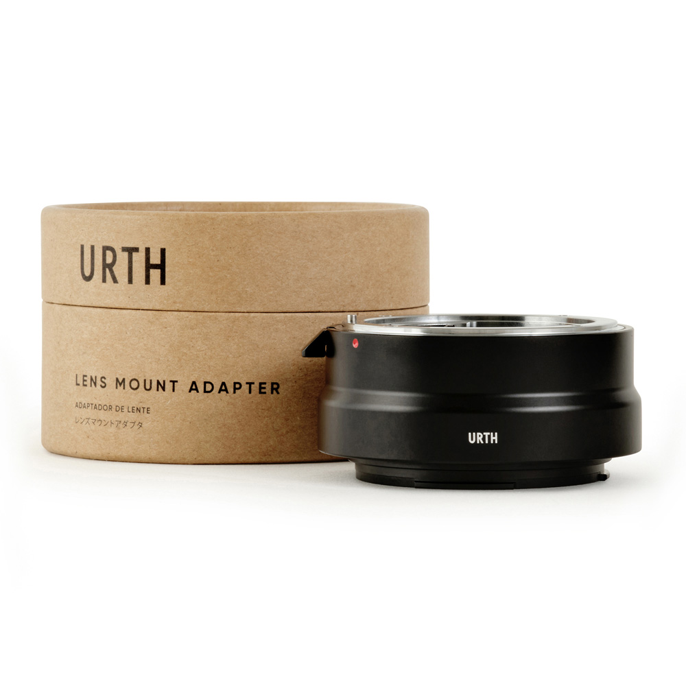 Musta Urth Nikon F - Canon RF objektiiviadapteri lepää sen sylinterimäisen ruskean pahvilaatikon vieressä, jossa lukee "Urth Lens Mount Adapter" englanniksi ja japaniksi.