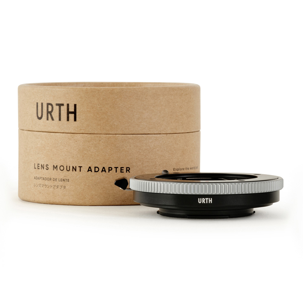 Urth Contax G - Fujifilm X objektiiviadapteri istuu sen lieriömäisen, ruskean pahvisen pakkauksen vieressä, jossa on merkintä "Lens Mount Adapter", ja molemmat näkyvät valkoisella pohjalla.
