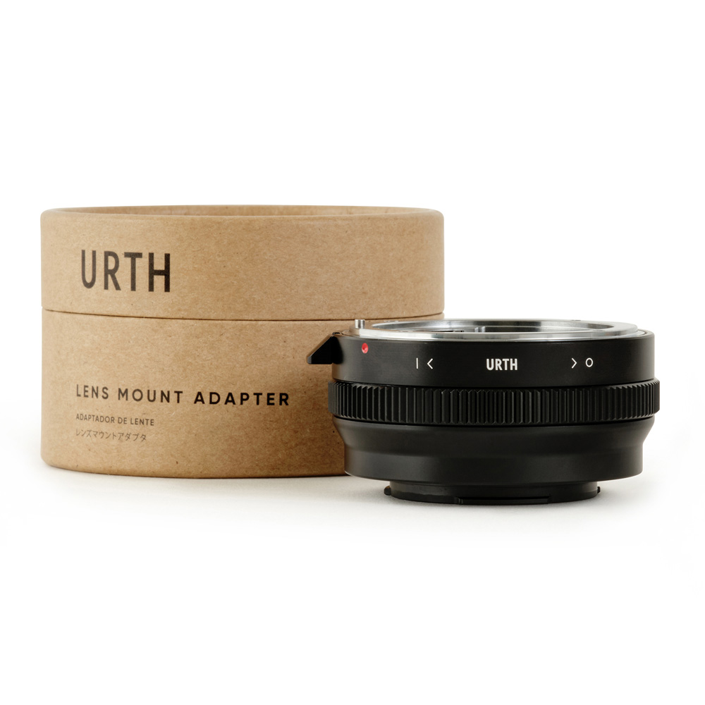 Musta Urth Nikon F (G-tyyppi) - Fujifilm X objektiiviadapteri näkyy sen sylinterimäisen ruskean pahvipakkauksen edessä, jossa lukee "URTH Lens Mount Adapter", kaikki valkoista taustaa vasten.