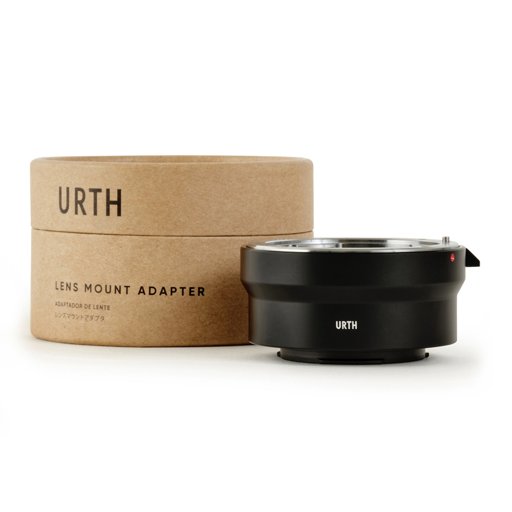 Musta Urth Pentax K - Fujifilm X objektiiviadapteri istuu sen ruskean lieriömäisen laatikon vieressä, jossa lukee "URTH Lens Mount Adapter" valkoista taustaa vasten.