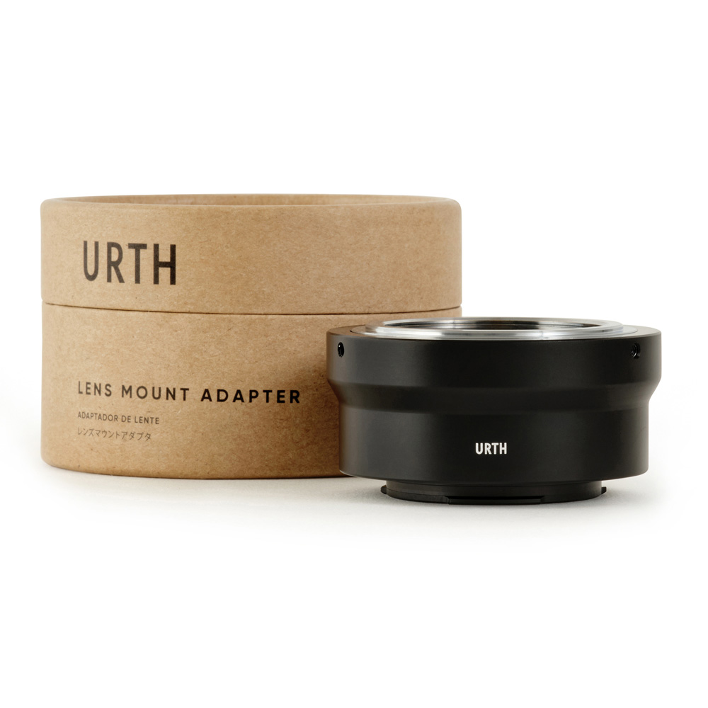 Musta Urth M42 - Fujifilm X objektiiviadapteri istuu sen sylinterimäisen pahvipakkauksen vieressä, jossa lukee "Lens Mount Adapter" ja "Urth" suurilla kirjaimilla valkoisella pohjalla.