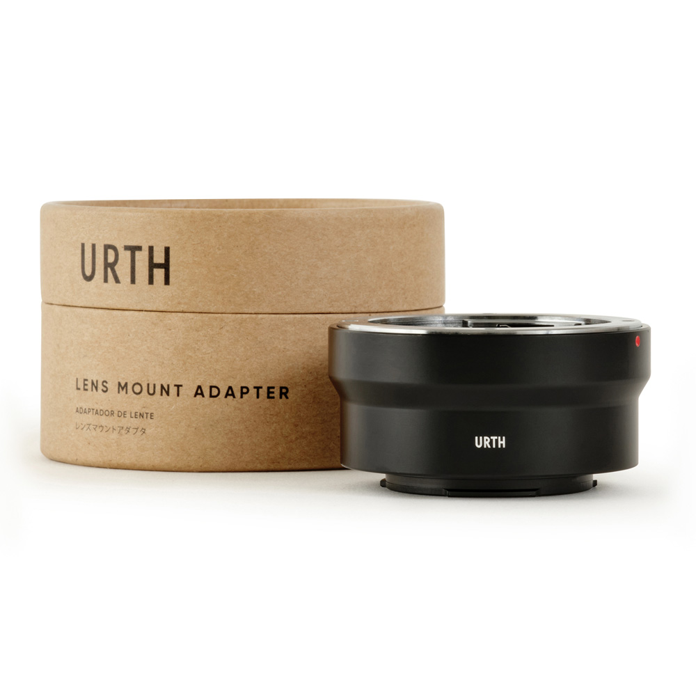Musta Urth Olympus OM - Fujifilm X objektiiviadapteri näkyy sen sylinterimäisen ruskean pahvipakkauksen vieressä, jossa on merkintä URTH Lens Mount Adapter; adapteri on tyylikäs ja kompakti.