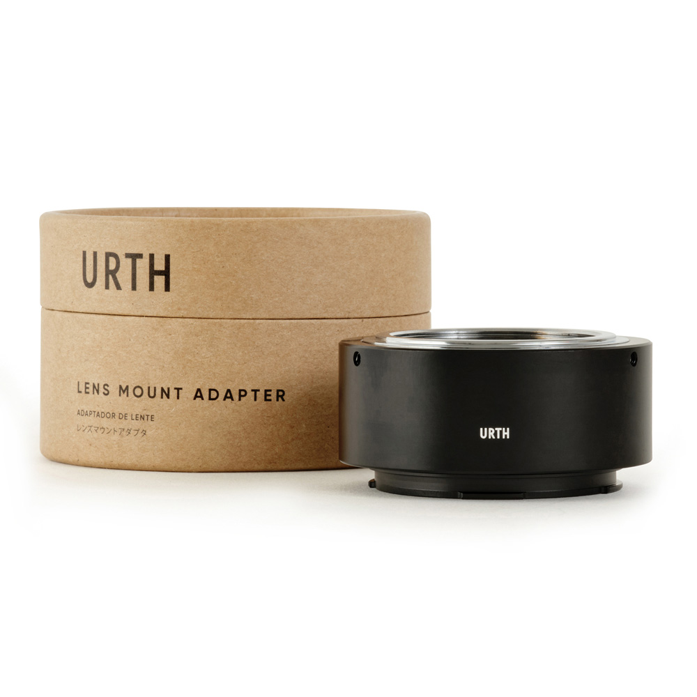 Musta Urth M42 - Leica L objektiiviadapteri istuu sen lieriömäisen ruskean pahvisen pakkauksen vieressä, jossa on merkintä URTH Lens Mount Adapter valkoisella pohjalla.