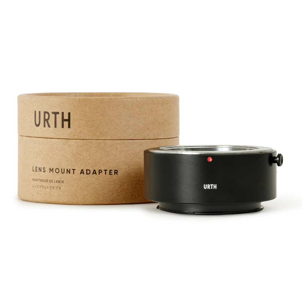 Sylinterimäinen laatikko, jossa lukee "Urth Minolta Rokkor (SR / MD / MC) - Leica L objektiiviadapteri", on mustan metallisen URTH-logolla varustetun objektiiviasennussovittimen vieressä, molemmat valkoista taustaa vasten.