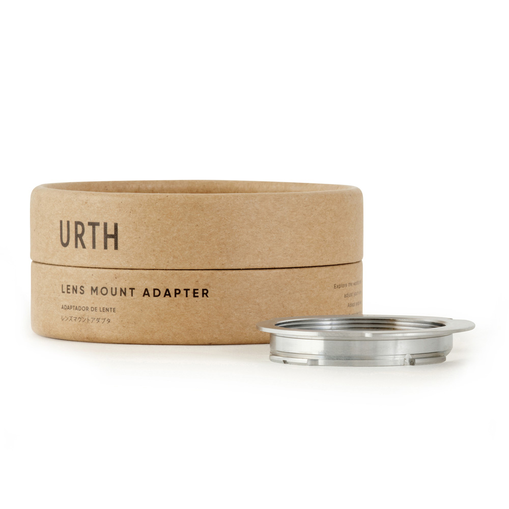 Metallinen Urth M39 - Leica M objektiiviadapteri (50 75mm Frame Lines) on esillä pyöreän, ruskean pahvilaatikon edessä, jossa on merkintä URTH Lens Mount Adapter valkoisella pohjalla.