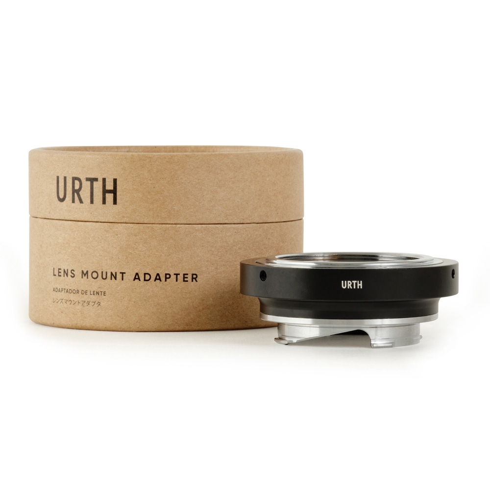The cylindrical cardboard box, which reads "Urth M42 - Leica M Lens Adapter", is next to a metal lens mount adapter, and both feature the Urth logo against a white background.