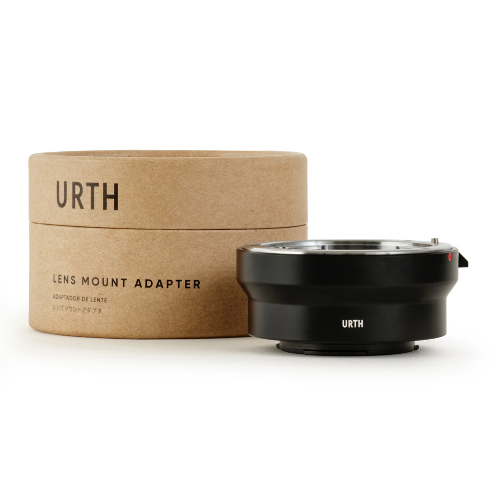 The Urth Pentax K - Micro Four Thirds (M4/3) lens adapter in black sits next to its brown, cylindrical Urth-branded box. This adapter allows Pentax K lenses to be attached to Micro Four Thirds cameras.