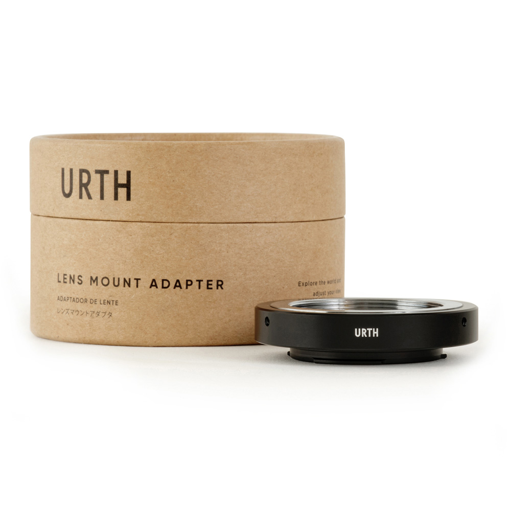 A brown cylindrical box with the words "Urth M39 - Micro Four Thirds (M4/3) lens adapter" is next to a black round adapter with "URTH" printed on it, and both are displayed on a white background.