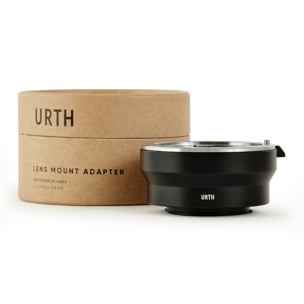 The black Urth Leica R - Micro Four Thirds (M4/3) lens adapter sits in front of its round, brown cardboard box, which reads "URTH LENS MOUNT ADAPTER" in bold.