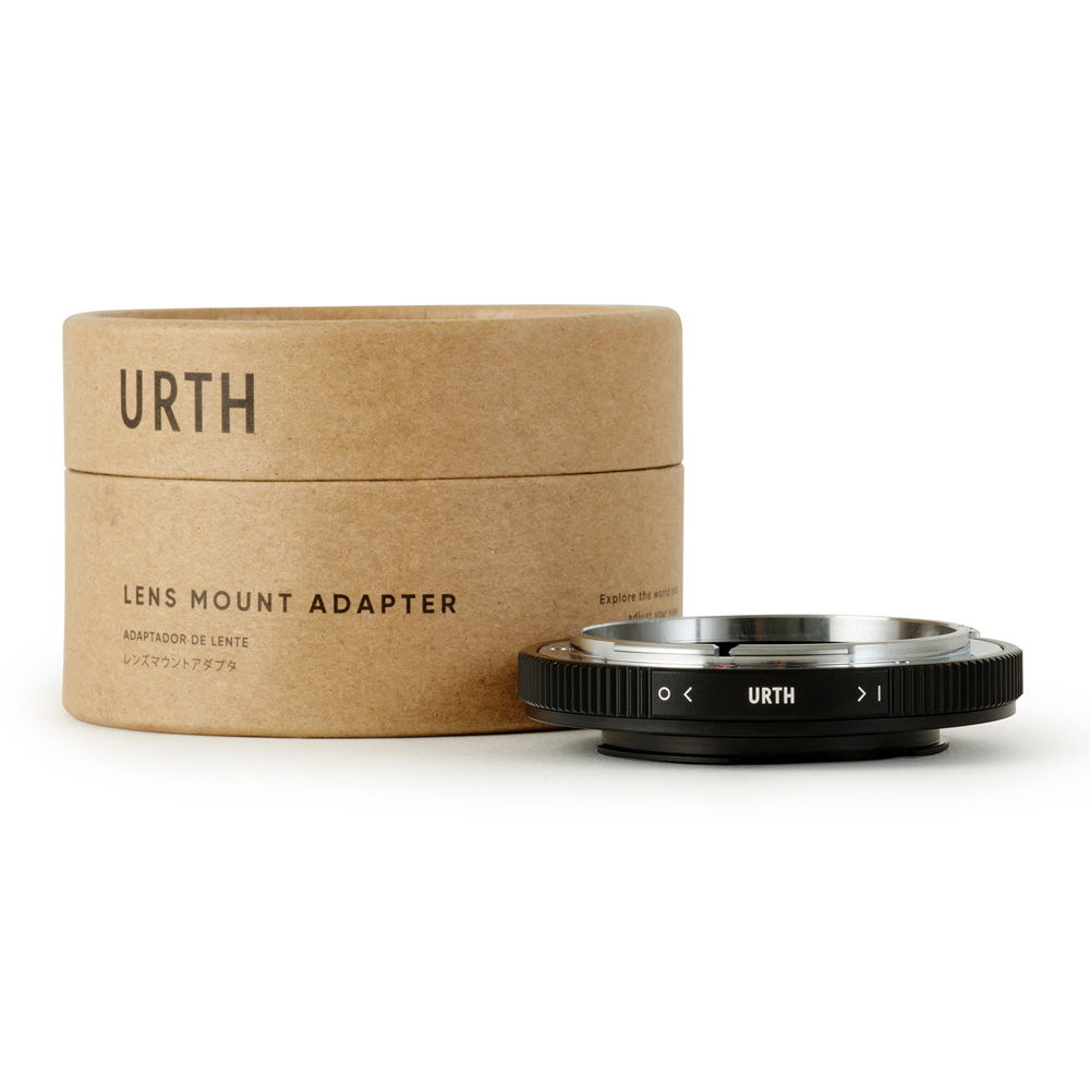 Urth Canon FD - Nikon F objektiiviadapteri (optisella lasilla) on esillä sen lieriömäisen pahvipakkauksen edessä, molemmissa on tuotemerkki ja tuotetiedot englanniksi ja japaniksi valkoisella pohjalla.