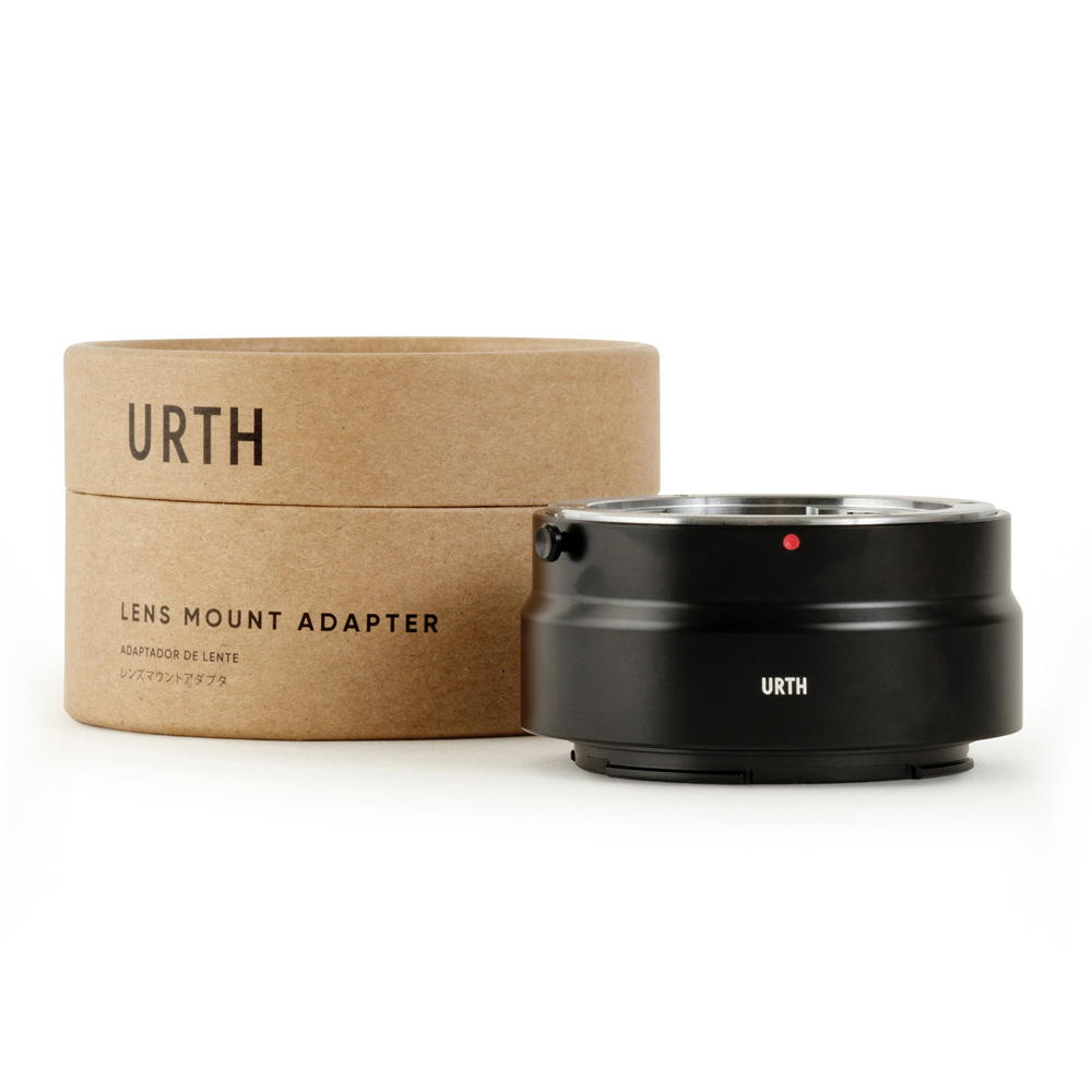 Musta Urth Contax/Yashica (C/Y) - Nikon Z objektiiviadapteri näkyy sen lieriömäisen ruskean pahvisen pakkauksen vieressä, jossa on merkintä "Urth Lens Mount Adapter" valkoisella pohjalla.