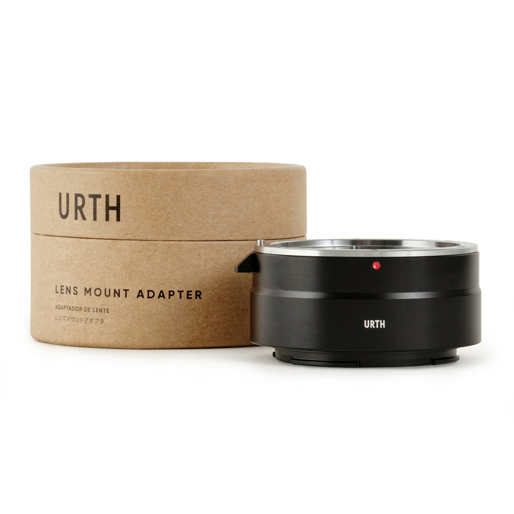 Musta Urth Canon (EF/EF S) - Nikon Z objektiiviadapteri istuu pyöreän, ruskean pahvilaatikon edessä, jossa lukee "Urth Lens Mount Adapter" mustalla tekstillä valkoisella pohjalla.