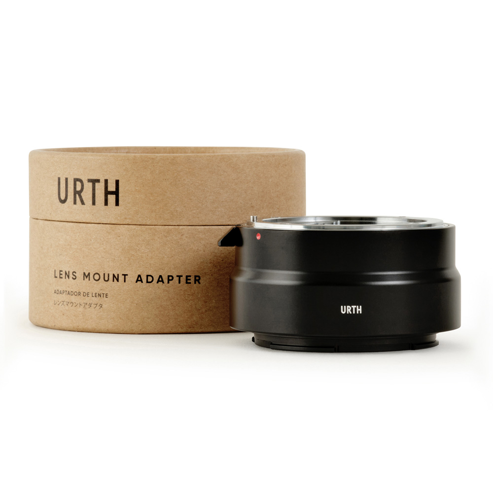 Musta Urth Nikon F - Nikon Z objektiiviadapteri istuu sen lieriömäisen pahvipakkauksen vieressä, jossa on merkintä URTH Lens Mount Adapter valkoista taustaa vasten.