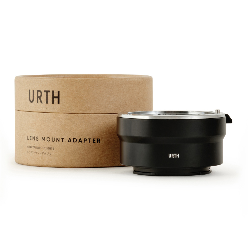 Musta Urth Leica R - Sony E objektiiviadapteri näkyy sen lieriömäisen ruskean pahvisen pakkauksen vieressä, jossa on merkintä URTH Lens Mount Adapter.