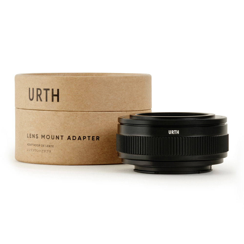 Musta Urth M42 - Sony E objektiiviasennussovitin (laajennettava) näkyy sen sylinterimäisen ruskean pahvilaatikon vieressä, jossa lukee englanniksi ja japaniksi "Urth Lens Mount Adapter".
