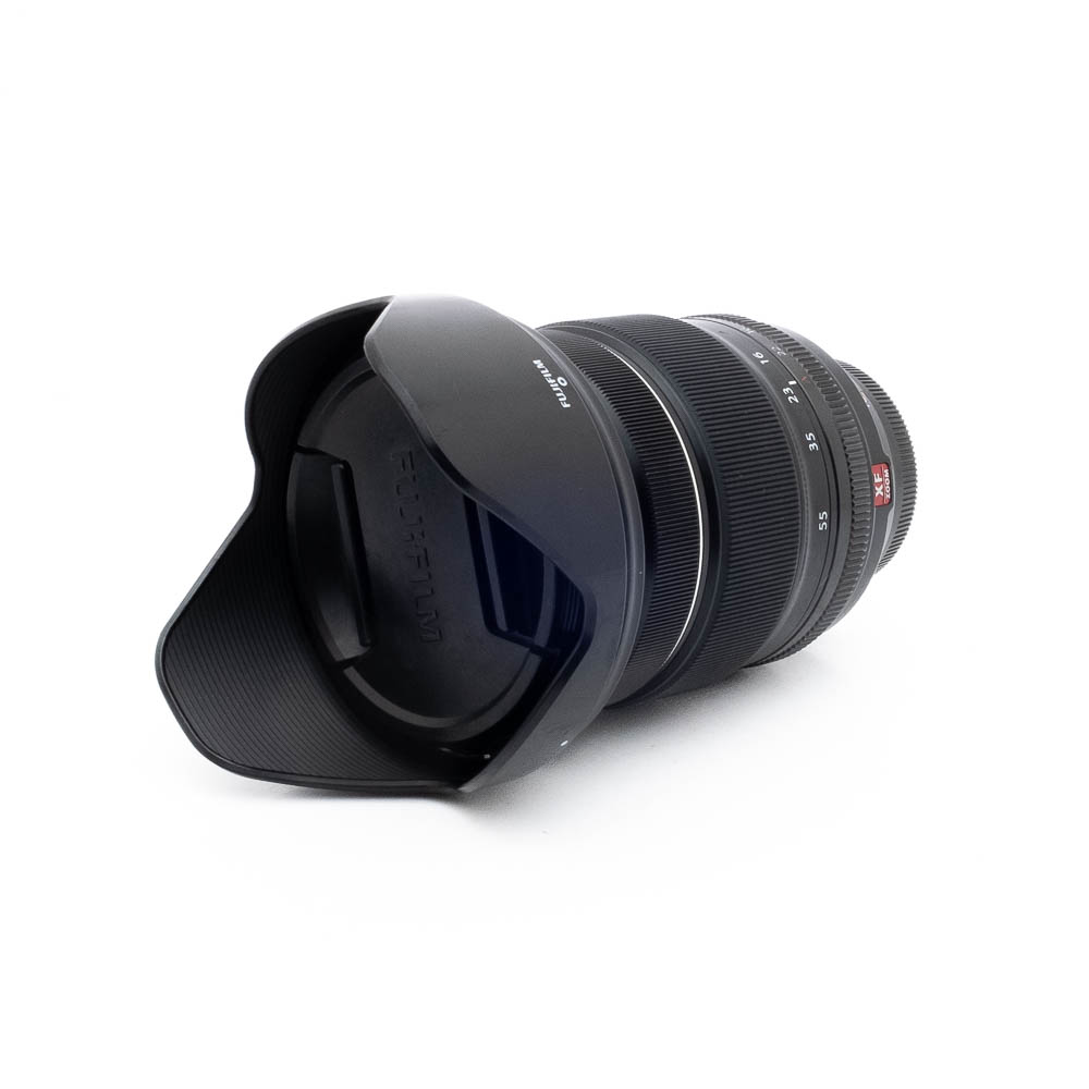 Fujinon XF 16-55mm f/2.8 R LM WR - Käytetty -objektiivi näkyy valkoisella taustalla, kun sen terälehden muotoinen vastavalosuoja on kiinnitetty, etuelementti ja vastavalosuoja on käännetty katsojaan päin.