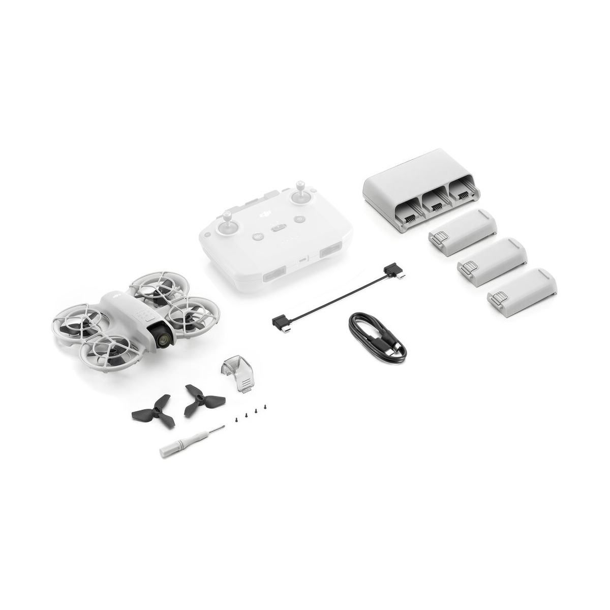 dji_neo_flymore_02 Valkoisella pinnalla esitelty DJI Neo Fly More Combo -dronipakkaus sisältää lennokin, kauko-ohjaimen, kolme akkua, latauskeskittimen, potkurit, ruuvimeisselin, ruuvit, USB-kaapelin ja pieniä sovittimia.
