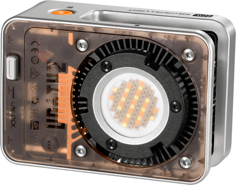 Zhiyun LED Molus X60 RGB Cob Light on kompakti, hopeanvärinen, suorakaiteen muotoinen paneeli, jonka läpinäkyvä kansi näyttää sen sisäosat ja keskeisen pyöreän LED-joukon. Siinä on näkyvät tuuletusaukot ja ohjauselementit helppokäyttöisyyttä varten.
