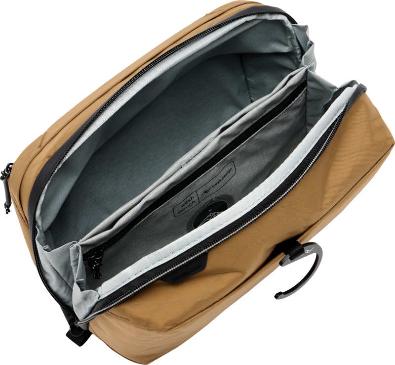 Peak Design Wash Pouch - Coyote on avattu, jolloin paljastuu tilava sisustus, jossa on useita harmaita ja mustia lokeroita ja taskuja, mukaan lukien pehmustettu holkki kannettavalle tietokoneelle tai tabletille.