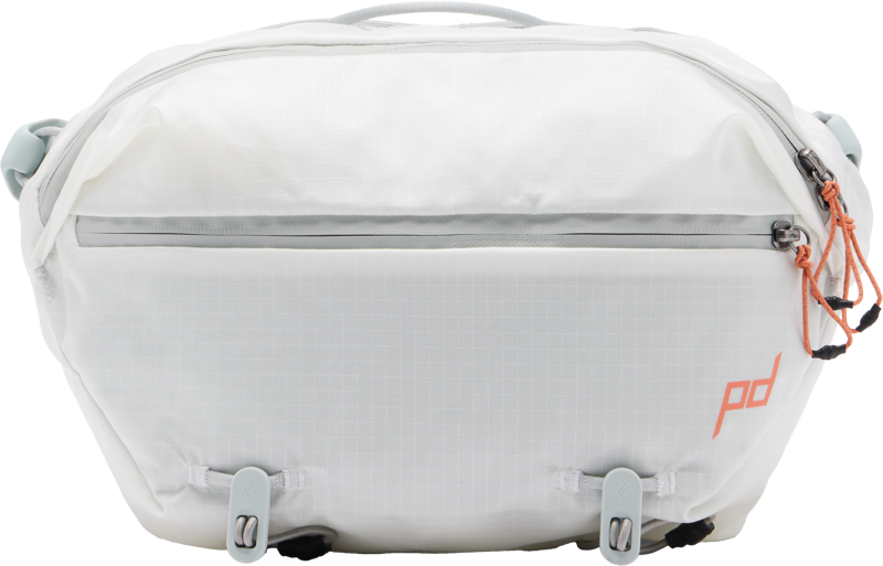 Peak Design Outdoor Sling 7L - Cloud on valkoinen rintareppu, jossa on harmaat korostukset, oranssit vetoketjunvetimet, vetoketjullinen etutasku, kaksi solkihihnaa ja oranssi PD-logo oikeassa alakulmassa.
