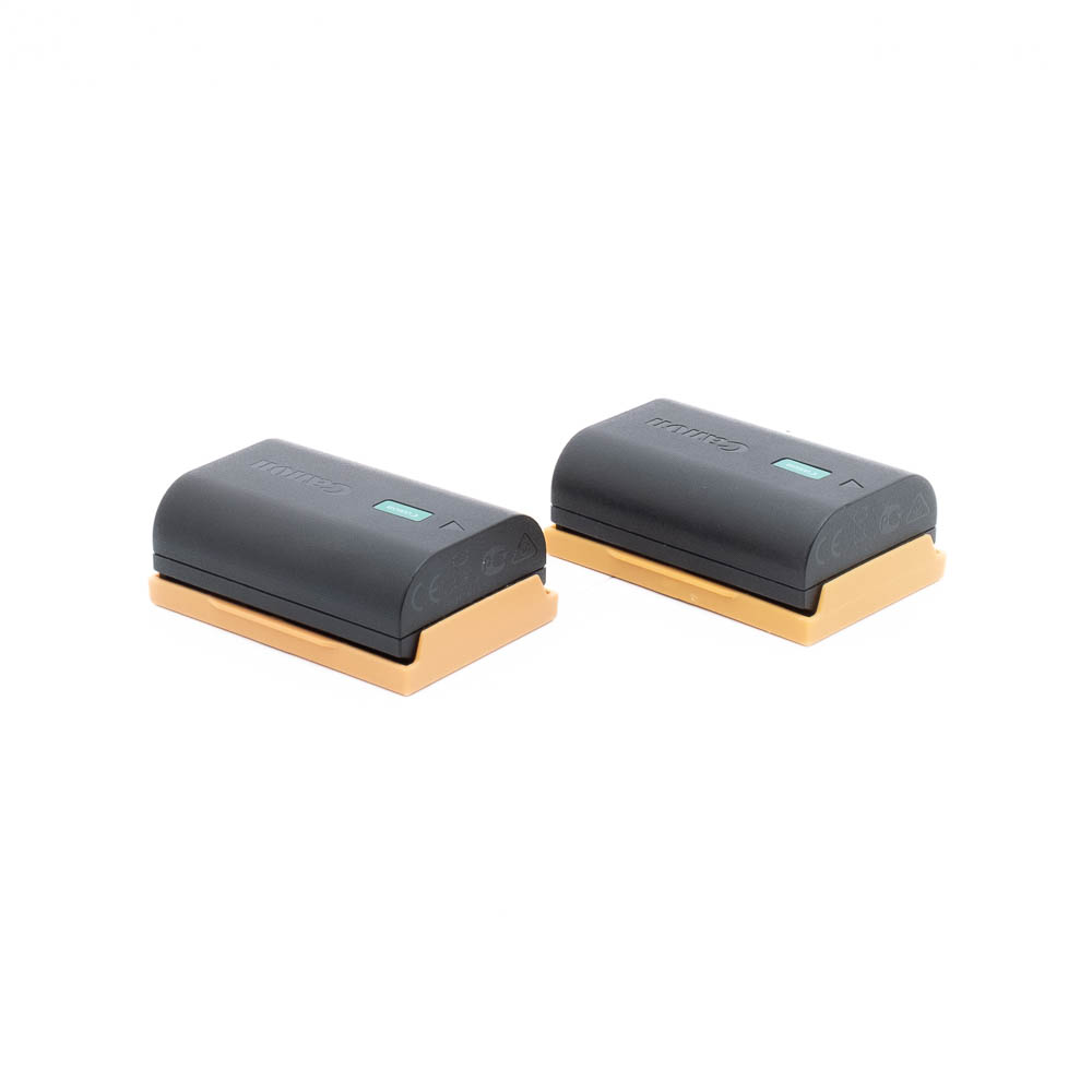 Two Canon LP-E6NH (incl.ALV25,5%) - Used battery in rectangular black case with gold base, side by side on white base.