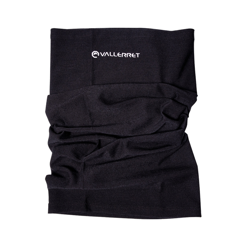 Vallerret Wool Neck Warmer (100 % merinovillaa), musta, jossa on valkoinen Vallerret-logo lähellä yläosaa, on kuvattu tasaisena valkoisella pinnalla. Pehmeä merinokangas näyttää hieman ryppyiseltä.
