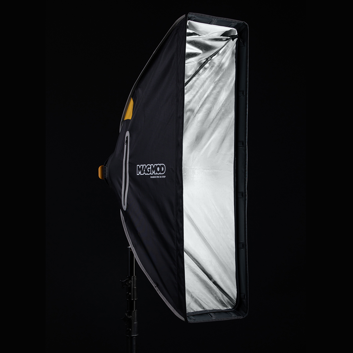 MagMod MagBox Pro 36 Strip, suorakulmainen softbox, jossa on heijastava hopeinen sisäpuoli, on asennettu valotelineeseen mustaa taustaa vasten valokuvausvalaistusta varten.