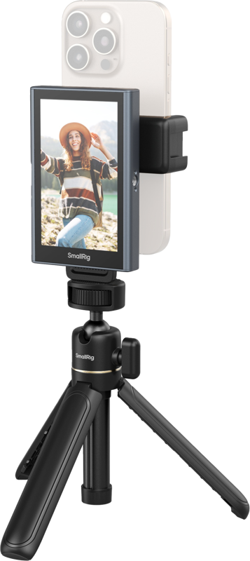 Hattupäinen nainen hymyilee ja poseeraa ulkona, kun hänen älypuhelimensa, joka on kiinnitetty SmallRig 4851 Wireless Video Monitor for Phone (Vlog Kit) -laitteeseen, näyttää hänen kuvansa näytöllä.