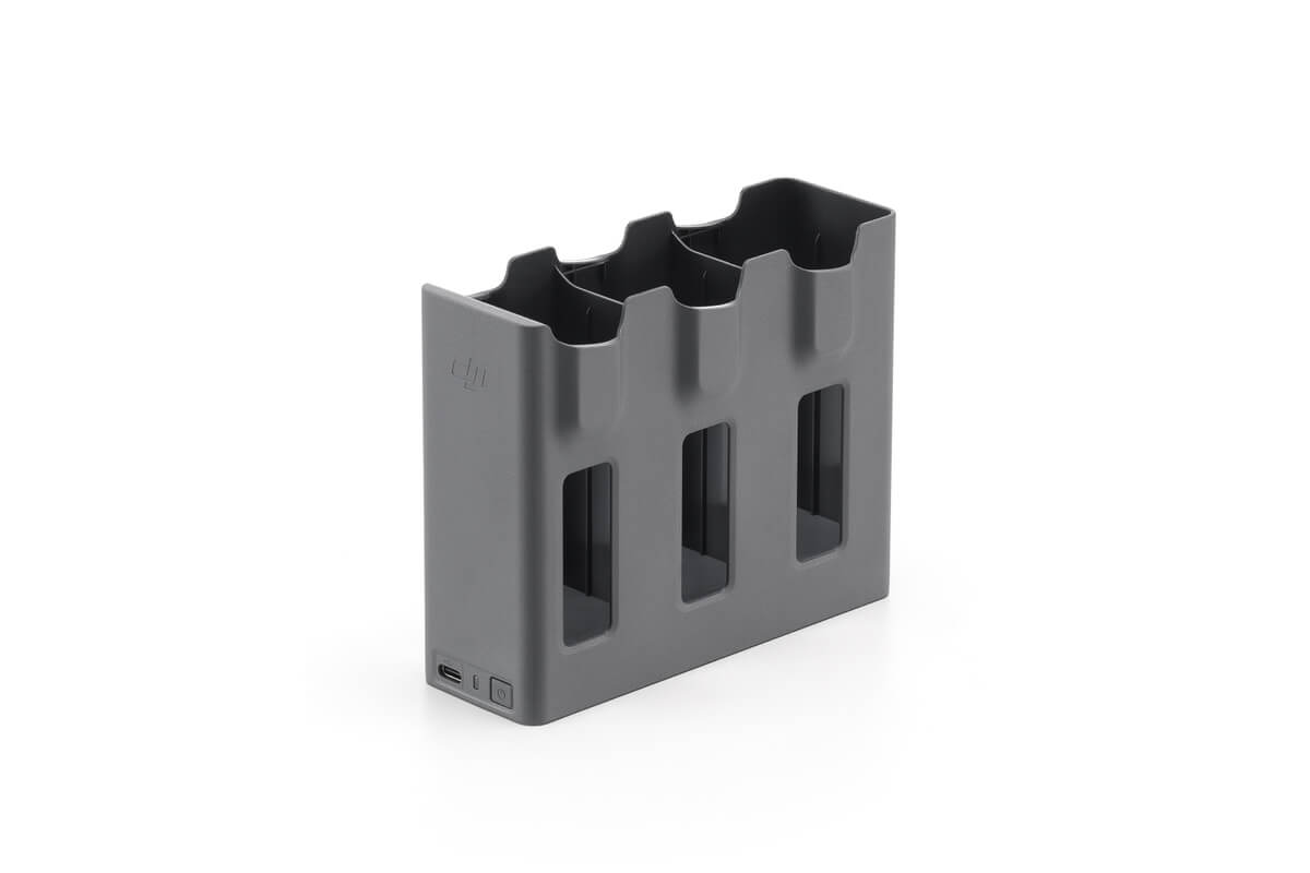 DJI Mavic 4 Pro Parallel Charging Hub -lataustelakka on harmaa, suorakulmainen latauskeskitin, jossa on kolme akkupaikkaa, joissa jokaisessa on pystysuuntaiset aukot, ja latausportti vasemmalla alhaalla, kuvassa tavallisella valkoisella pohjalla.