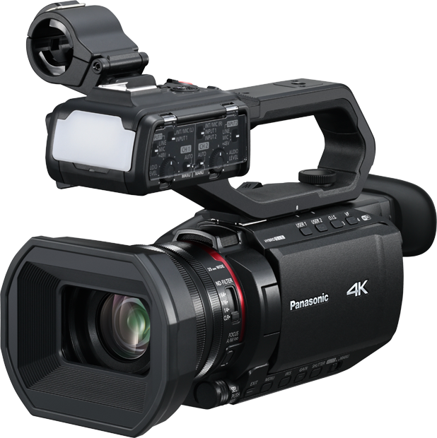 Mustassa Panasonic AG-CX18EJ -videokamerassa on suuri objektiivi, yläkahva, ulkoinen mikrofonikiinnike ja liitetyt äänisäätimet, jotka näkyvät vaalealla taustalla.
