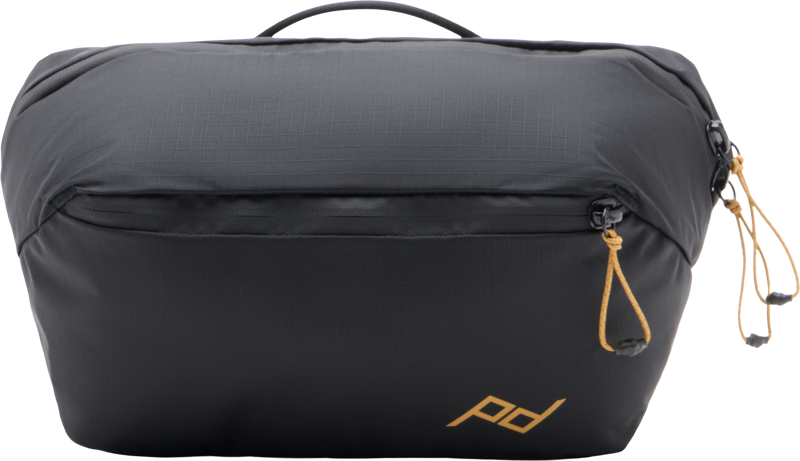 Peak Design Outdoor Sling 4L Black on musta vetoketjullinen pussi, jossa on yläkahva, kultaiset vetoketjunvetimet oikealla ja kultainen "pd" -logo oikeassa alakulmassa.