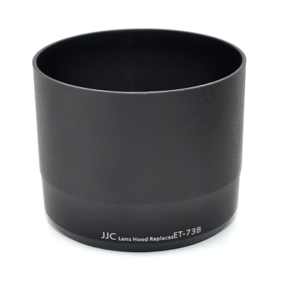 Musta lieriömäinen JJC ET 73B Canon -vastavalosuoja Musta mattapintainen linssinsuojus, jossa on valkoinen painatus "JJC Lens Hood Replaces ET-73B" lähellä pohjaa, kuvassa valkoista taustaa vasten.