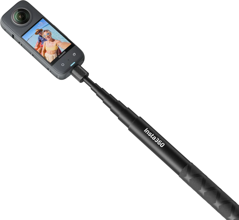 Insta360 114cm Invisible Selfie Stick mustassa värissä, johon on kiinnitetty 360 asteen toimintakamera, näyttää kaksi hymyilevää ihmistä näytöllään rannalla.
